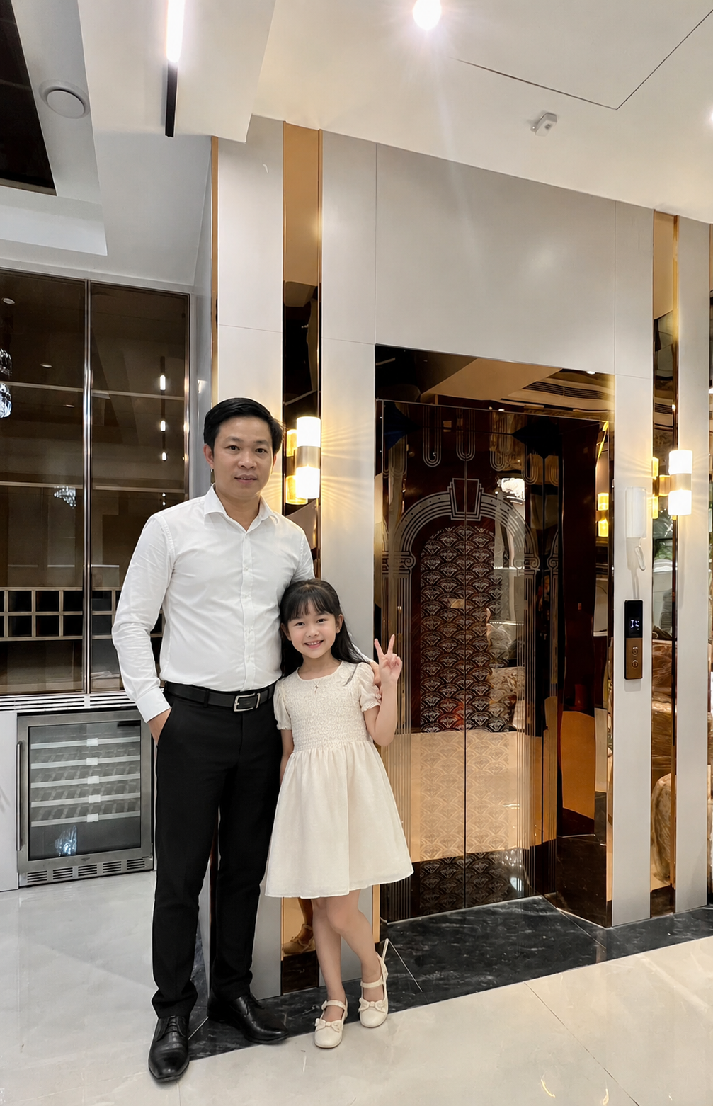 Hai cha con đứng trước cửa thang máy kính sang trọng trong sảnh tòa nhà hiện đại